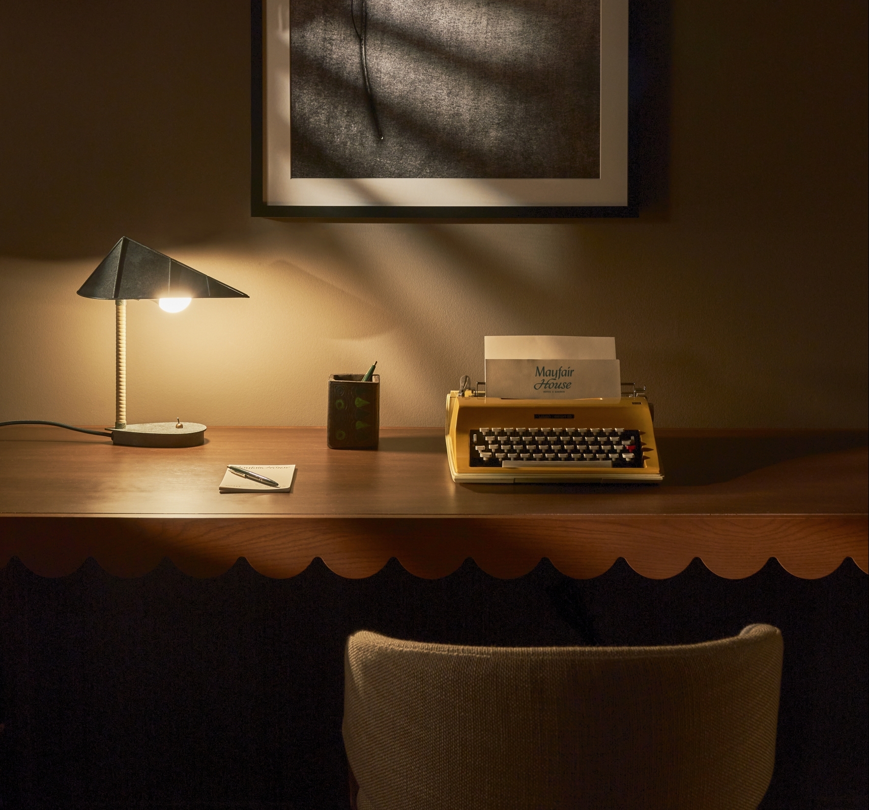 A desk with a lamp, typewriter, and notebook in a room.