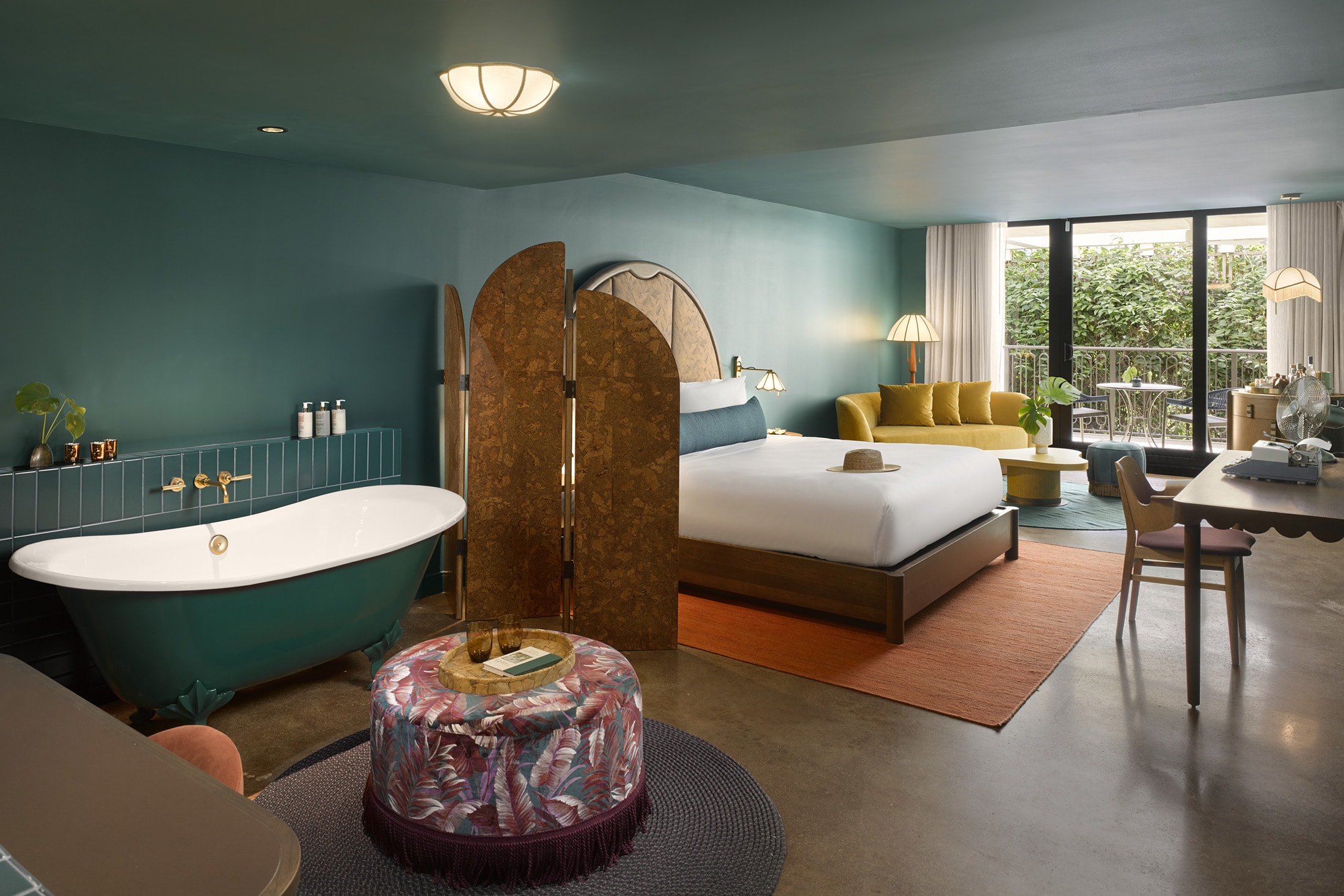 A wide view of a hotel room with a bathtub, bed, sofa, table, and chair.