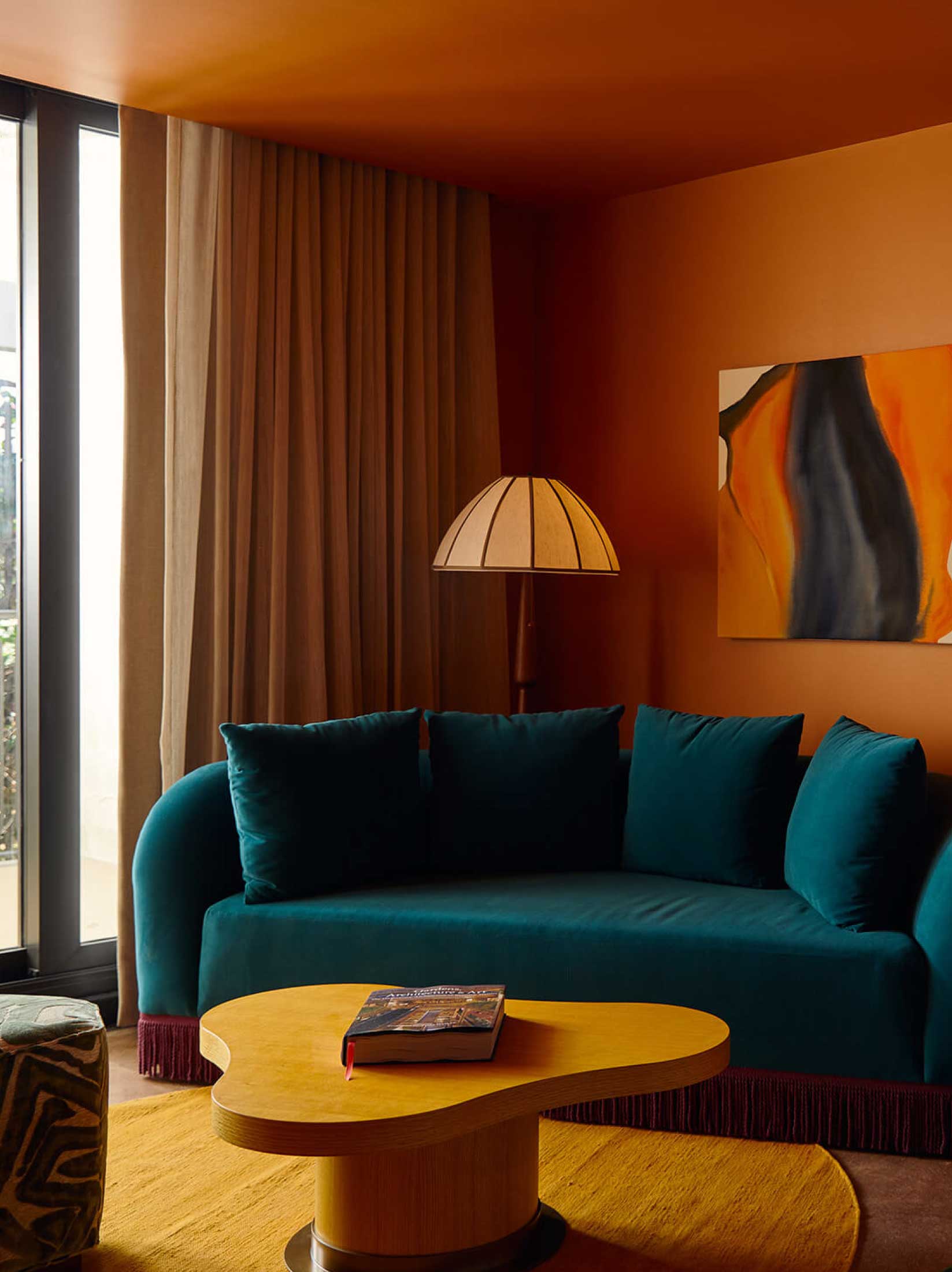 A teal sofa and wood coffee table sit in a cozy lounge area with abstract art on the wall.