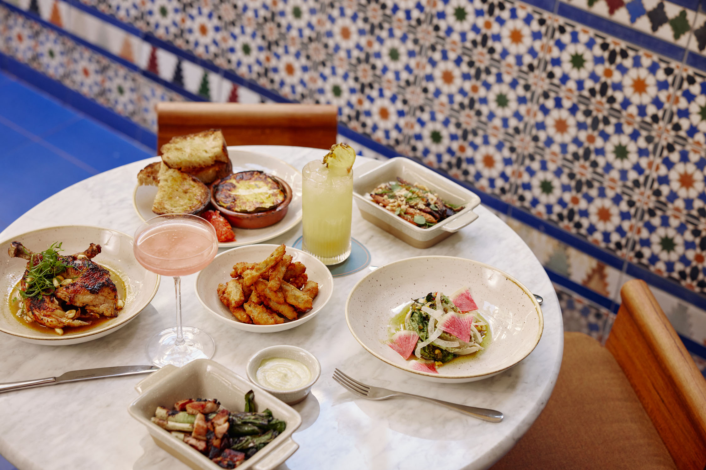 A table set with various dishes and drinks in a restaurant with a tiled wall.