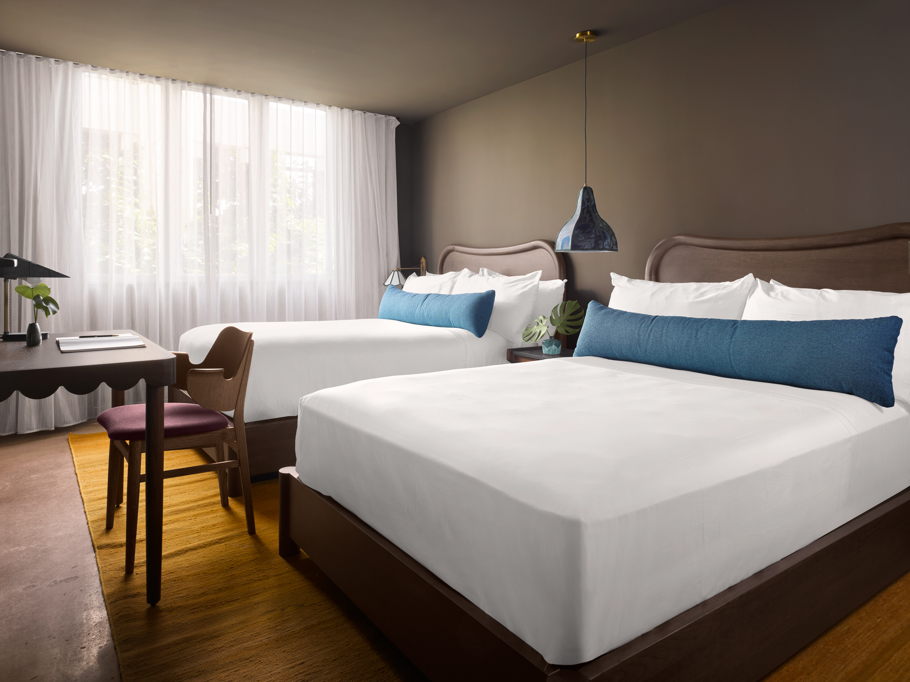 A hotel room with two beds, a desk, and a chair.