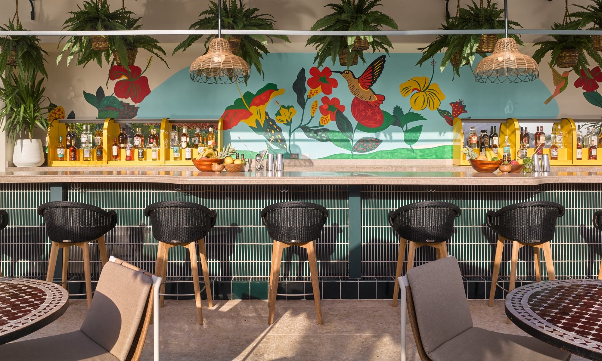 a bar with a colorful mural, stools, and plants