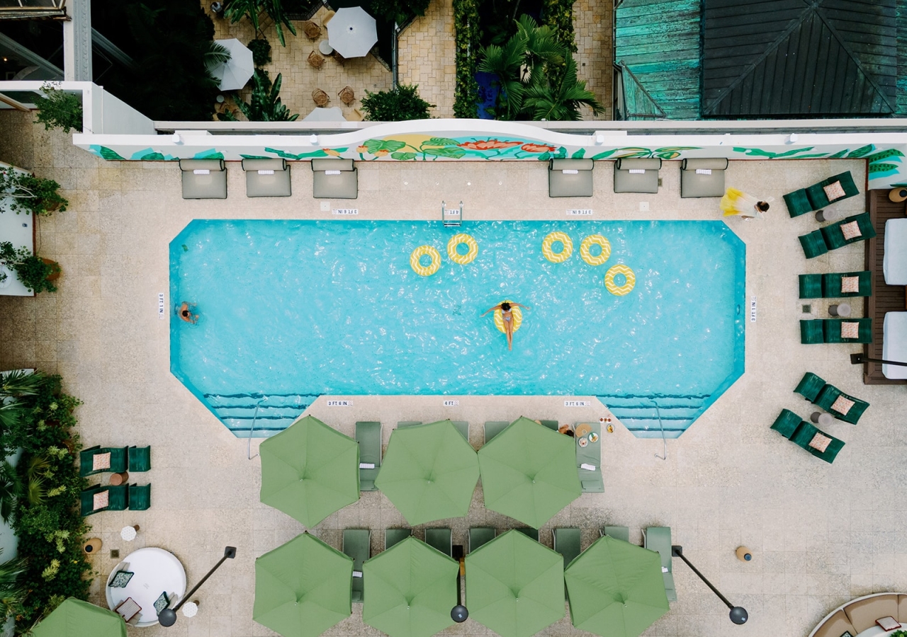 An aerial view of a pool with green umbrellas and lounge chairs around it.