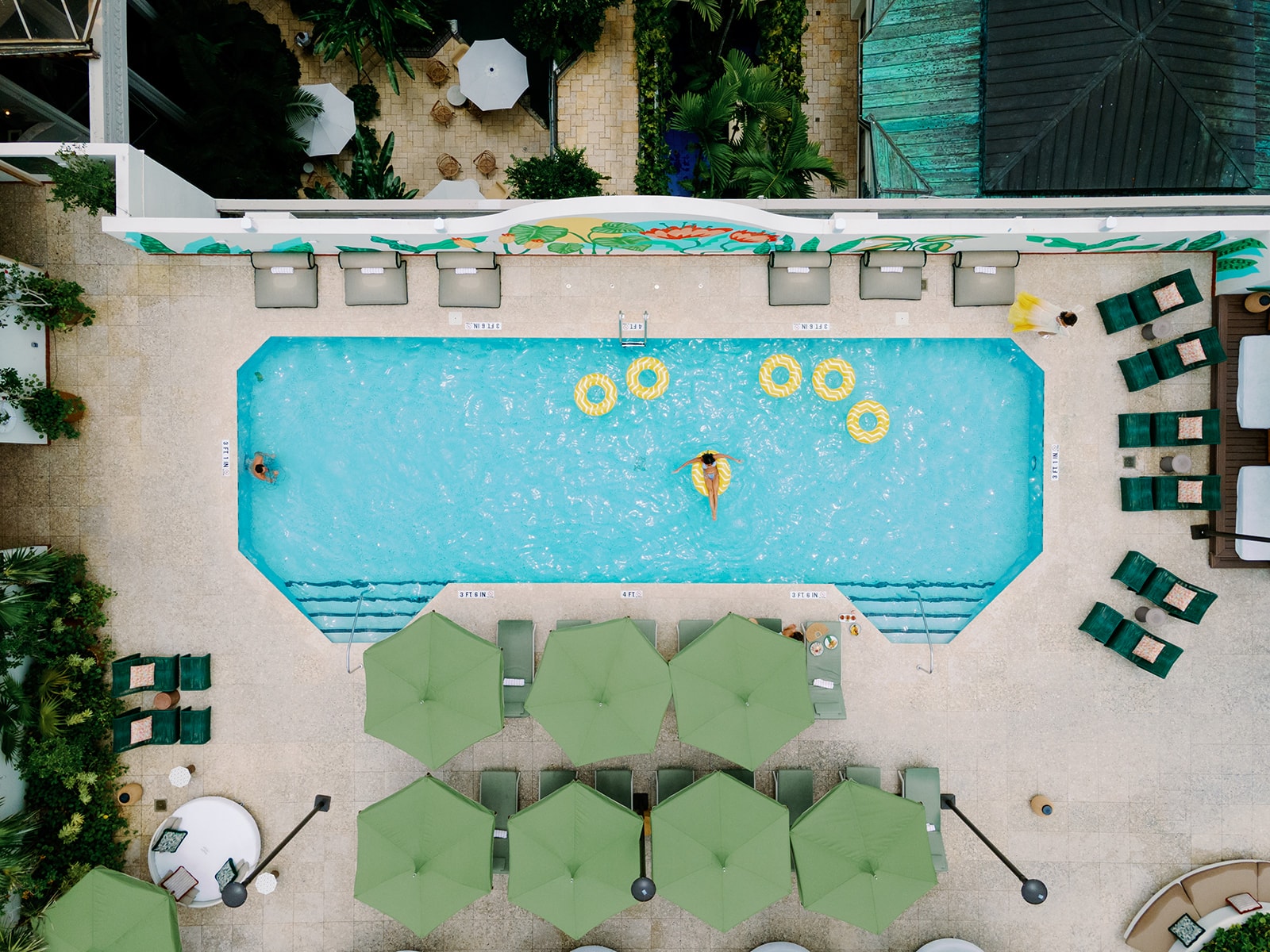 An aerial view of a pool with green umbrellas and lounge chairs around it.