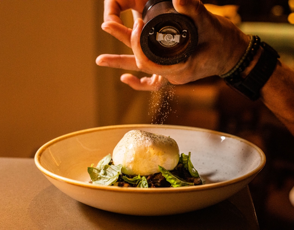 Someone shakes pepper over a dish