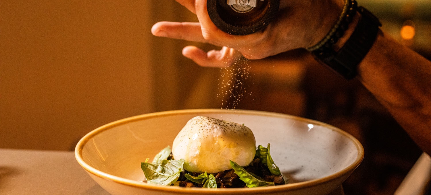 Someone shakes pepper over a dish