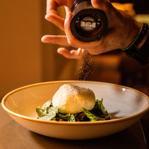 Someone shakes pepper over a dish